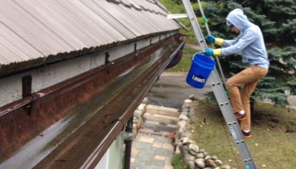 man on a ladder cleaning his gutters alone