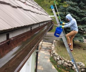 man on a ladder cleaning his gutters alone
